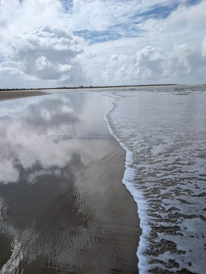 Clouds reflected in wet sand where the tide runs in