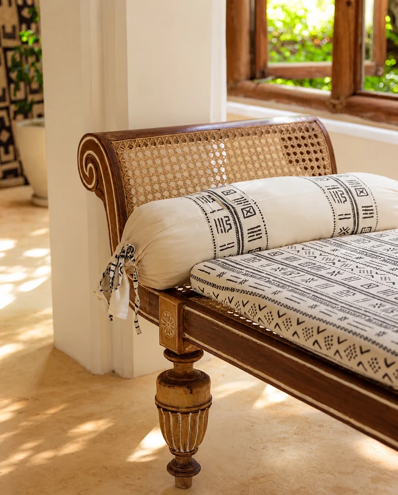 A caned day bed with a scrolled arm and carved, turned legs, dressed with printed cushions and a bolster