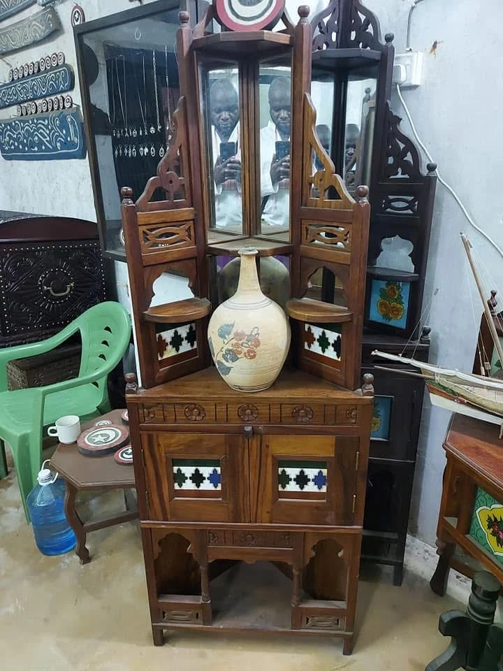 A carved corner display cabinet with mirrors and patterned tiles, holding a hand-painted vase