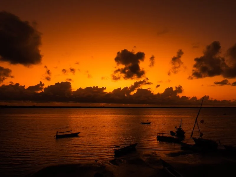 Small boats on still water under a fiery sunset