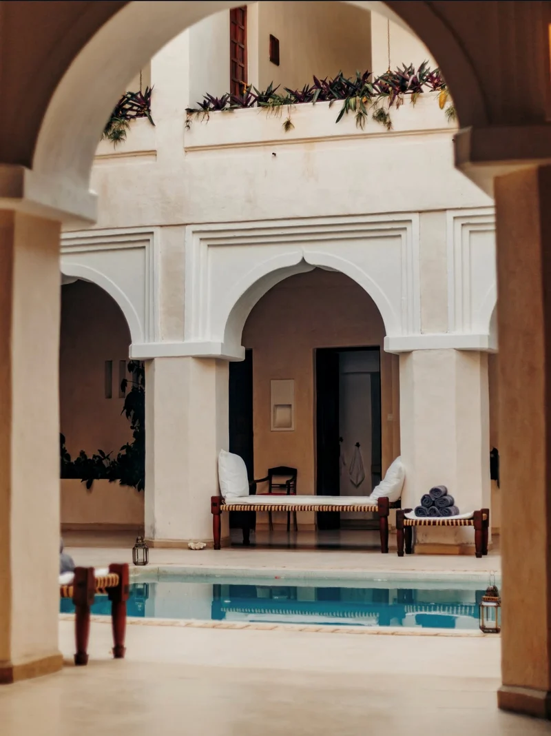 A carved Swahili arcade opening onto the pool, a day bed and side table beneath the arches