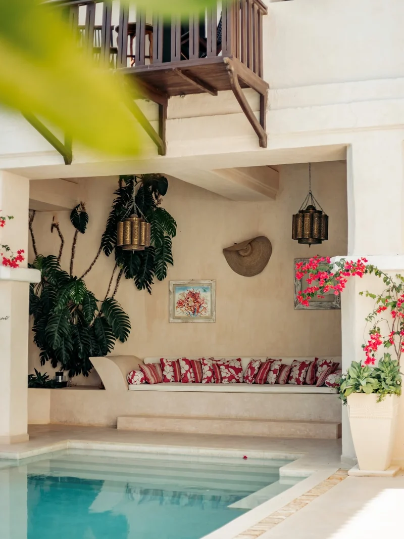 A built-in baraza seat with red patterned cushions and brass lanterns beside the pool