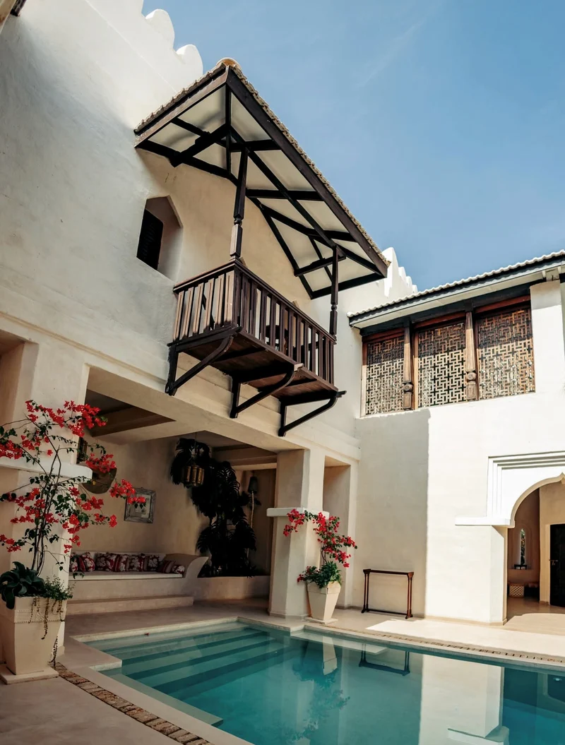 A whitewashed courtyard with a carved timber balcony, bougainvillea and a plunge pool